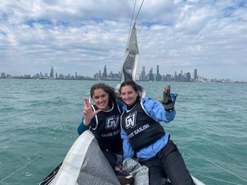 GV sailors give the "Anchor Up" sign on the bow of a boat, backed by the Chicago skyline